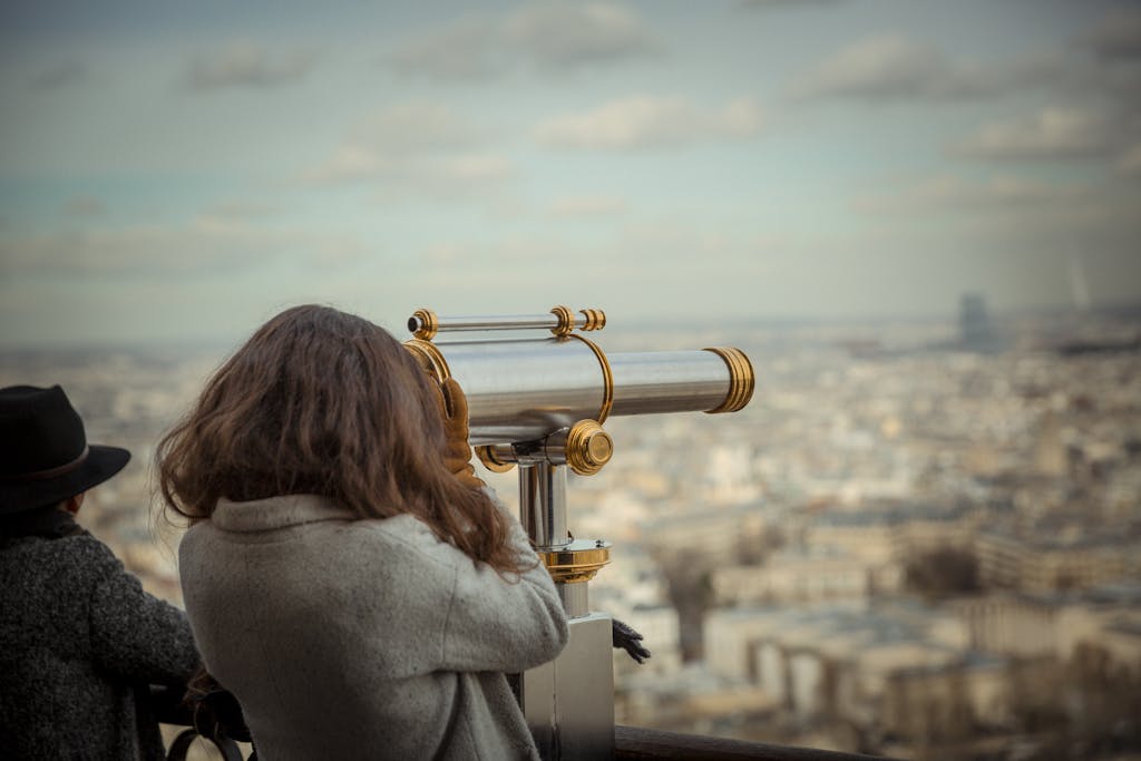 A woman uses a telescope to observe a sprawling cityscape during the day.